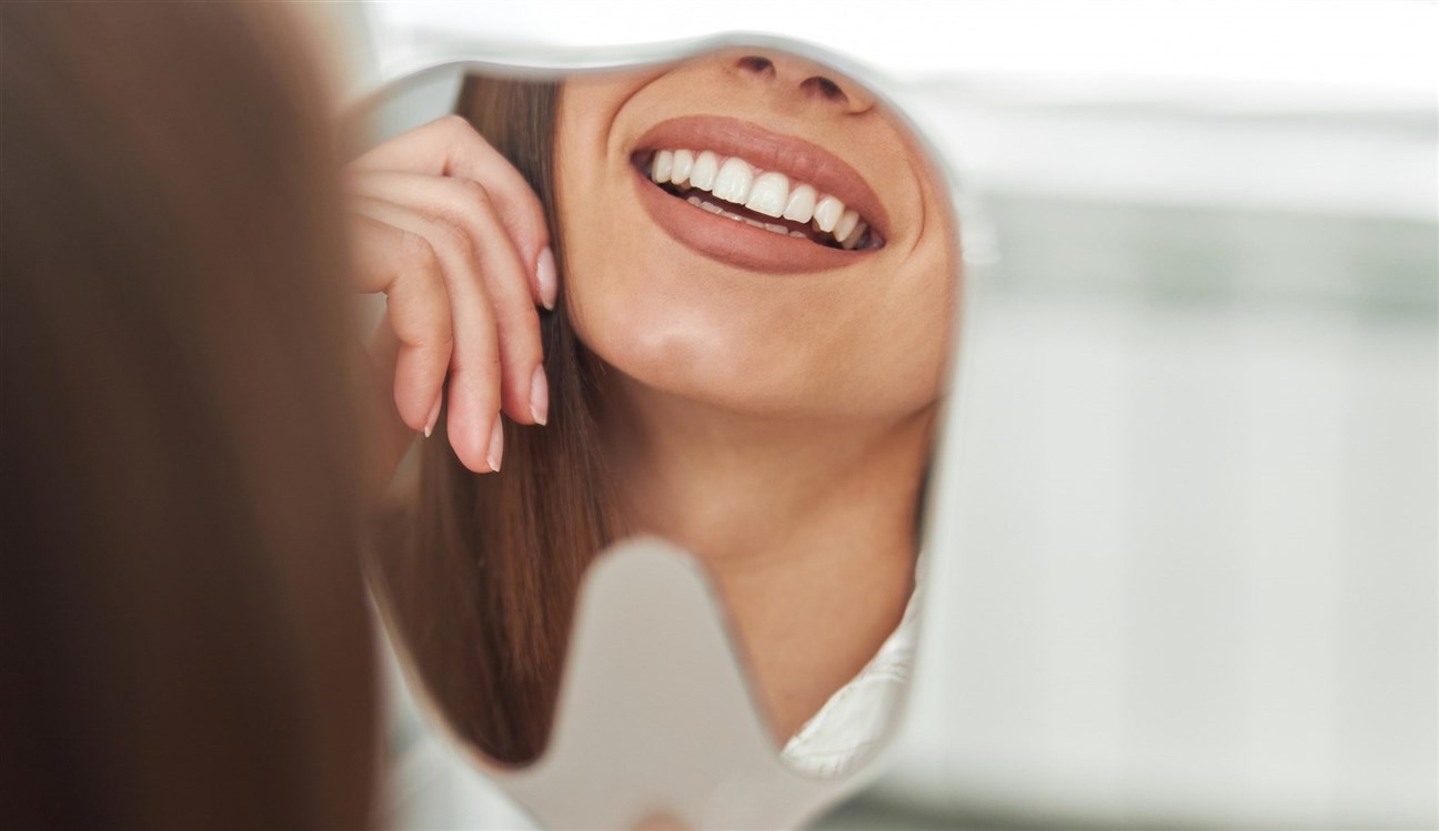 happy-young-woman-smiling-checking-out-her-perfect-healthy-teeth-mirror-close-up-dentist-office240122042457313~
